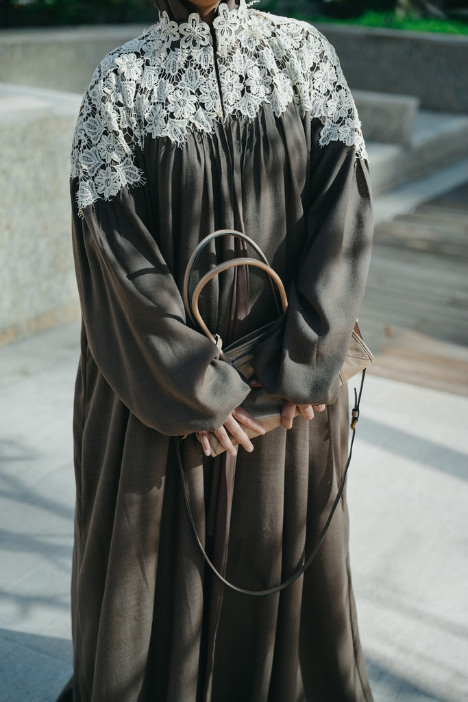 Model wearing a coco brown linen abaya featuring crochet lace, high neck, and pleated puff sleeves.