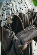 Load image into Gallery viewer, Model wearing a coco brown linen abaya featuring crochet lace, high neck, and pleated puff sleeves.
