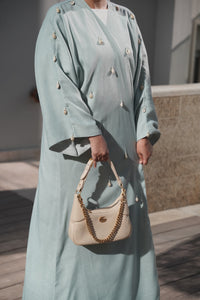 Detail shot of Aquatic Marine linen bisht abaya featuring hand-sewn seashells on the sleeves and front bodice.
