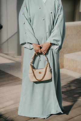 Detail shot of Aquatic Marine linen bisht abaya featuring hand-sewn seashells on the sleeves and front bodice.